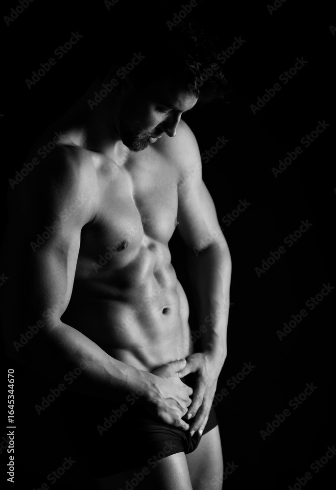 Naklejka premium Handsome bodybuilding man posing shirtless on black background flexing muscles and six pack after a workout
