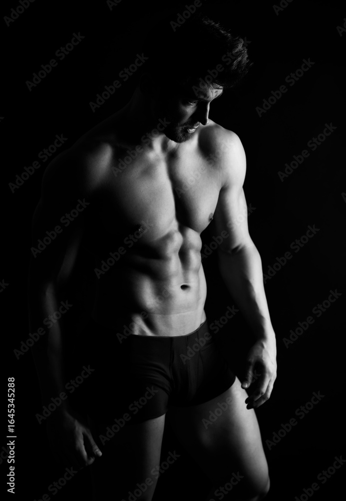 Naklejka premium Handsome bodybuilding man posing shirtless on black background flexing muscles and six pack after a workout