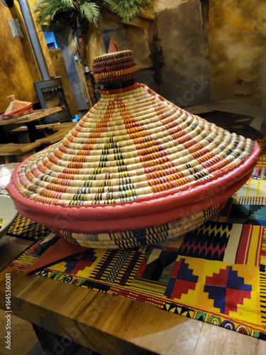 Traditional Ethiopian woven injera basket (mesob) on colorful tablecloth in ethnic restaurant