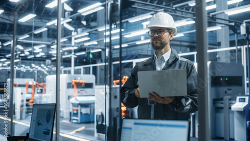 Wallpaper Mural Factory Office: Portrait of Confident Caucasian Male Chief Engineer Wearing Hard Hat Working on Laptop Computer. Technician At Automated Robot Arm Assembly Line Manufacturing Electronic Components. Torontodigital.ca