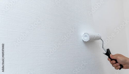 Close-up of a person's hand using a paint roller to apply fresh white paint to a textured wall, concept of home renovation and DIY.