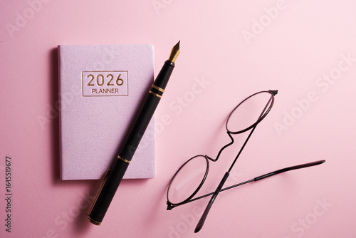 2026 planner,pen and eyeglasses against pink background.
