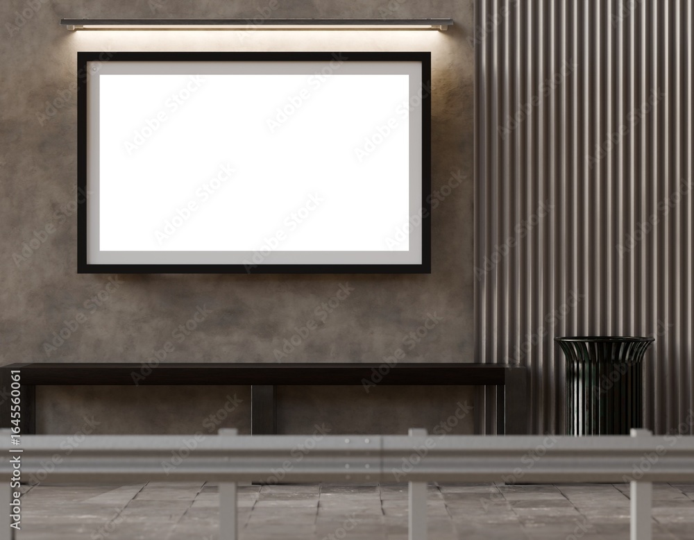 A blank rectangular poster hangs above a dark bench against a textured wall with vertical metal slats and a small trash receptacle; a low barrier is in the foreground A blank rectangular poster hangs above a dark bench against a textured wall with vertical metal slats and a small trash receptacle; a low barrier is in the foreground