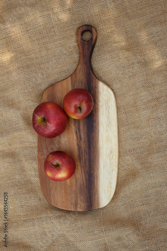 Three red apples on a wooden cutting board