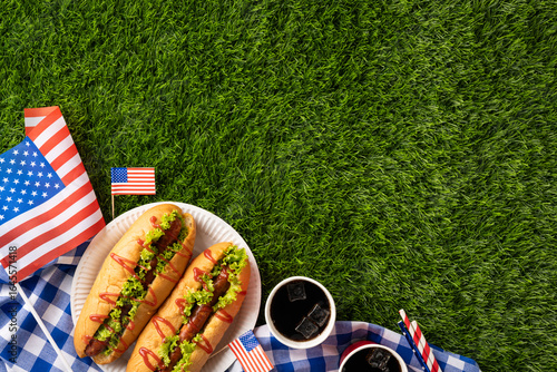 Obraz na płótnie Independence Day picnic setting featuring hot dogs, American flags, and grass ba
