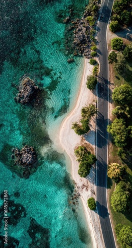 Overhead view of a tropical coast turquoise water, white sand beach curving gently, a road lined with palm trees runs parallel