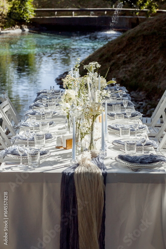 served table, glasses, plates, vase with forge, In nature by the lake