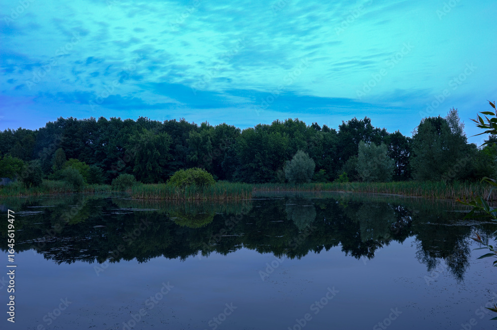 Obraz premium Calm summer evening, dusk after sunset on a forest lake. Harmonious widescreen panoramic side view of the shore, overgrown with trees. Harmony of HDR style.
