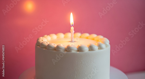White cake with single candle on top against soft pink background, celebrating special occasion, perfect for birthday, party, or festive event decoration