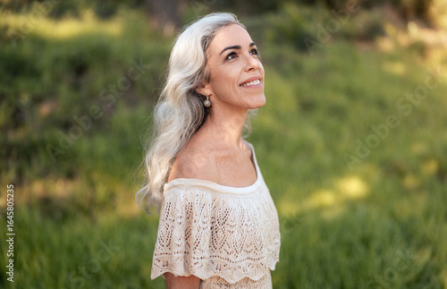 Wall Mural A woman with long grey hair smiles peacefully while enjoying the serene outdoors in a sunny park setting