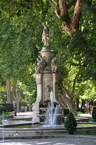 Madrid, Spain - September 5 2010: Side view of the Apollo Fountain on Madrid's Paseo del Prado, with a lush green backdrop created by surrounding trees