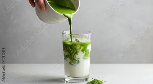 A hand pours matcha latte over ice into a glass.