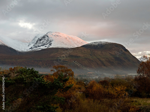 Autumn sun going down on Ben Nevis and the lower outlier Meall an t-Suidhe above misty Fort William, seen from Camaghael,  Highlands of Scotland.