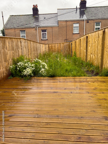 Plymouth Devon England UK. 07.06.2025. Garden fencing with new wooden decking surrounds a small patch of grass