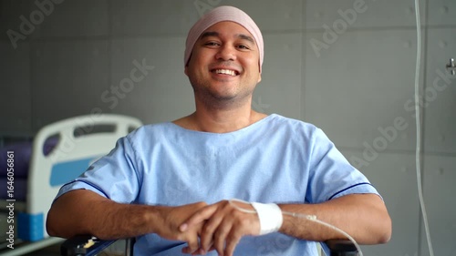 Smiling young patient man with cancer in headscarf happy with chemotherapy treatment result and looking at camera in the hospital room, prevention for cancer and health awareness on world cancer day.