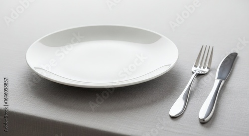 An empty white ceramic plate with a silver fork and knife set on a gray tablecloth.