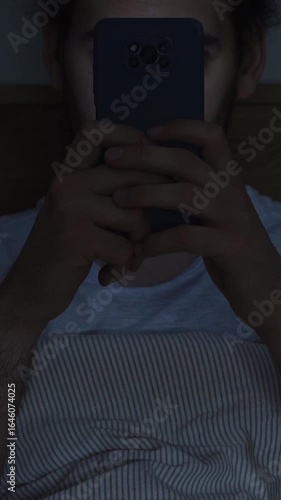 Smartphone and social network addiction concept. Young male using smartphone in bed at night