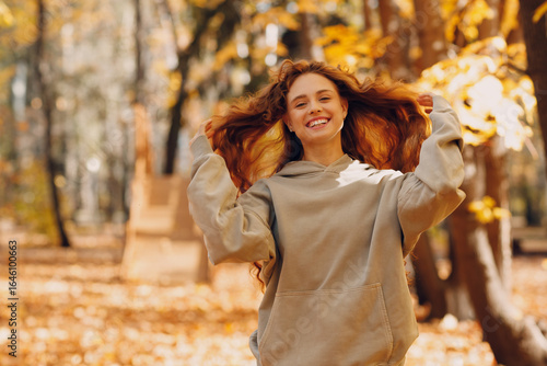 Smiling young woman with curly hairstyle enjoys the autumn weather in the forest with the yellow leaves at sunset