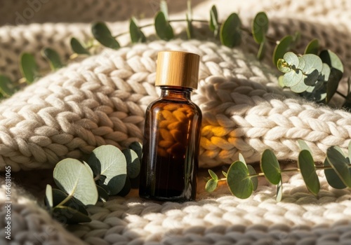 Amber Glass Bottle with Gold Cap and Eucalyptus on Knitted Blanket