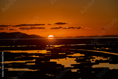 First light breaks over Lake Titicaca, painting the waters and Andes in hues of gold and rose — a serene awakening at the world’s highest navigable lake. Puno Peru.