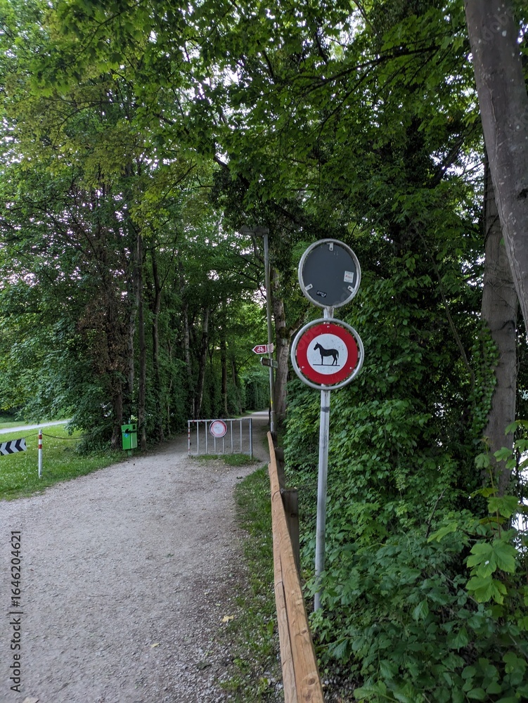 Naklejka premium Pathway in a lush green environment with traffic signs indicating restrictions. Ideal for concepts of nature, outdoor activities, or rural settings.