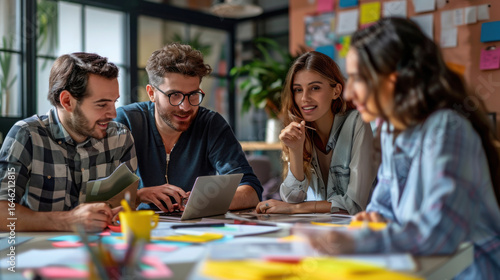 Four young professionals collaborating on a laptop in a modern office environment together closely