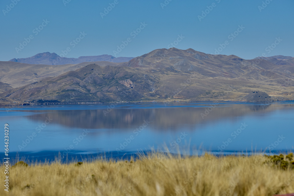 Obraz premium Deep blue waters embrace golden highland hills at Lagunillas Lake near Puno — a serene Andean sanctuary of beauty and calm