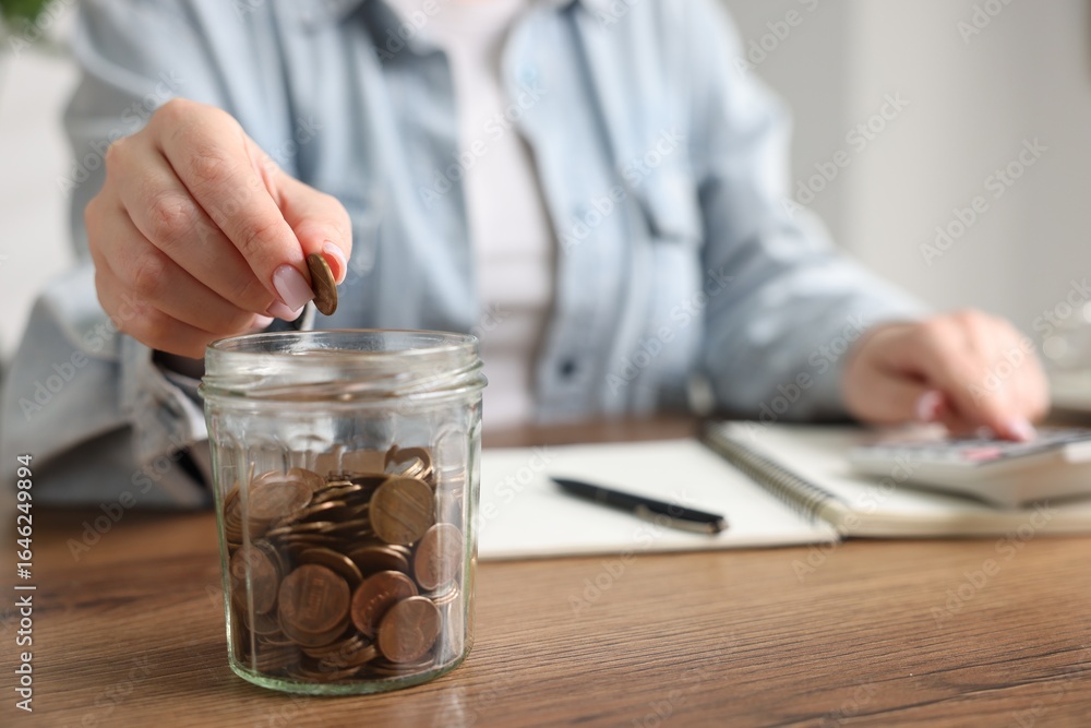 Fototapeta premium Woman counting and putting coins into jar at wooden table, selective focus