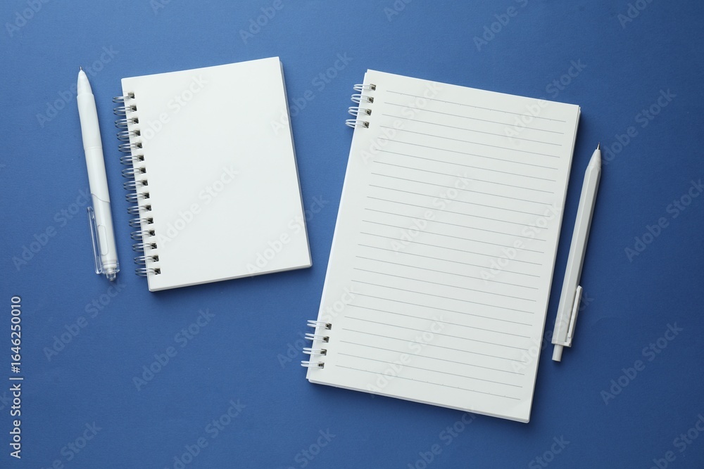 White notebooks and pens on blue background, flat lay