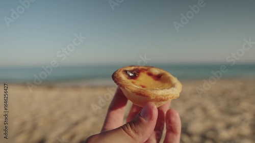 Hand holding Portuguese custard tart with ocean view, Algarve, Portugal