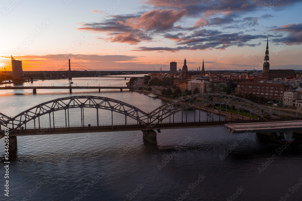 Fototapeta premium Riga, Latvia at sunset with the Daugava River, Railway Bridge, Riga TV Tower, and old town spires of St. Peter's Church and Riga Cathedral.