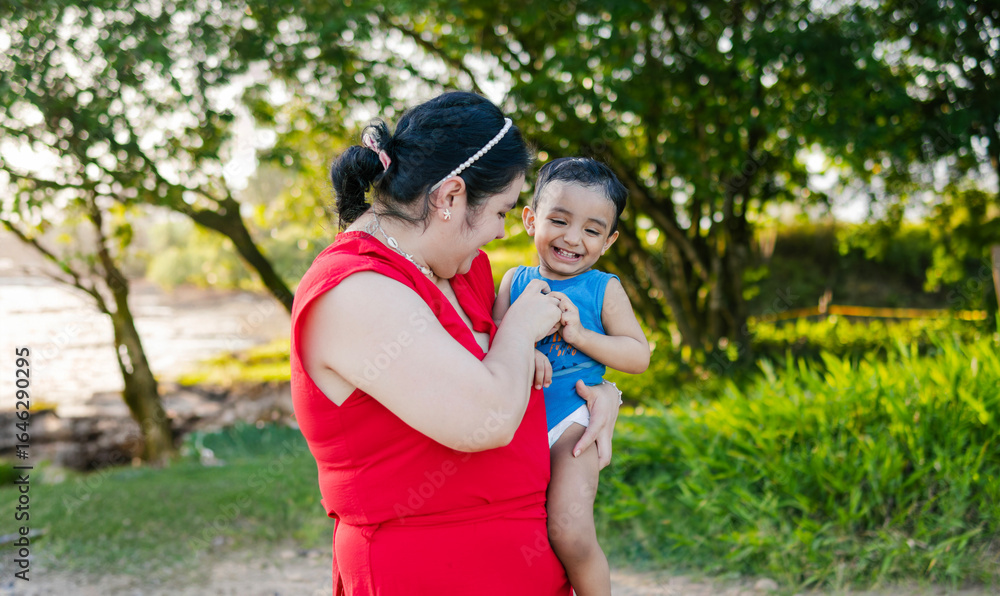 Fototapeta premium Mother tenderly hugs her young son while sharing a moment together on the riverbank during summer vacation.