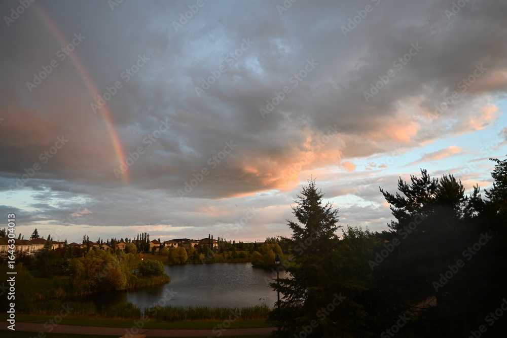 A rainbow sitting above a suburban pond, with a cloudy sky after rain. Taken from a backyard A rainbow sitting above a suburban pond, with a cloudy sky after rain. Taken from a backyard
