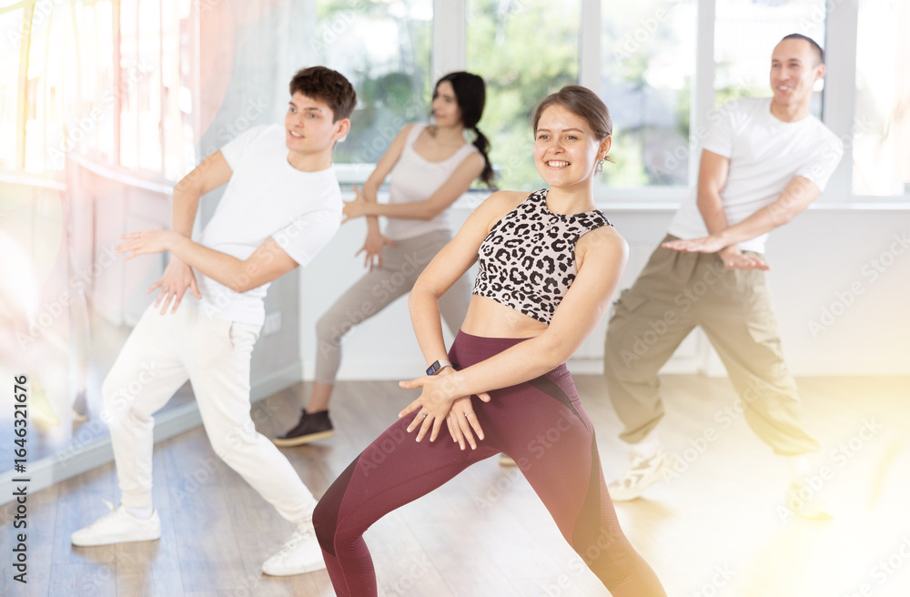 Obraz premium Positive expressive young woman learning modern street dancing during group class in choreographic studio..
