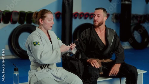 Man and woman Brazilian Jiu-Jitsu athletes sitting and talking in gym and taking selfie