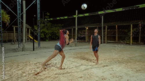 Two people beautiful woman and handsome brazilian man playing beach volleyball at night on sand court