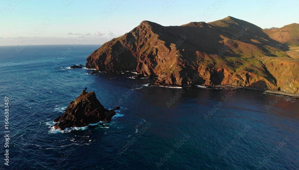 Fototapeta premium Dramatic coastal cliffs and a solitary rock formation rise from the deep blue ocean under a clear sky.
