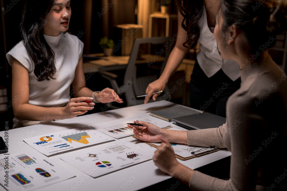 Fototapeta premium Asian businesswomen working late analyzing financial charts in office meeting room