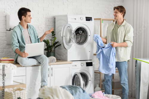 Male students with laptop doing laundry in dormitory