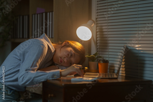 Фототапет Young Asian office worker falling asleep at workplace with laptop and calculator