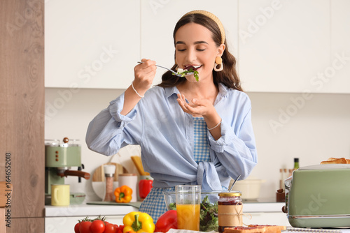 Young woman eating vegetable salad at table in kitchen