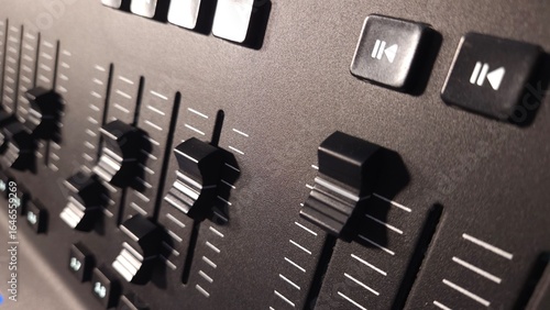 Close-up view of fader sliders and control buttons on a professional lighting control panel.