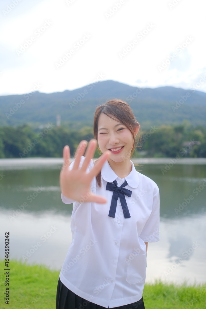 Fototapeta premium A girl in a white shirt and black skirt is posing for a picture by the water. A Student girl concept