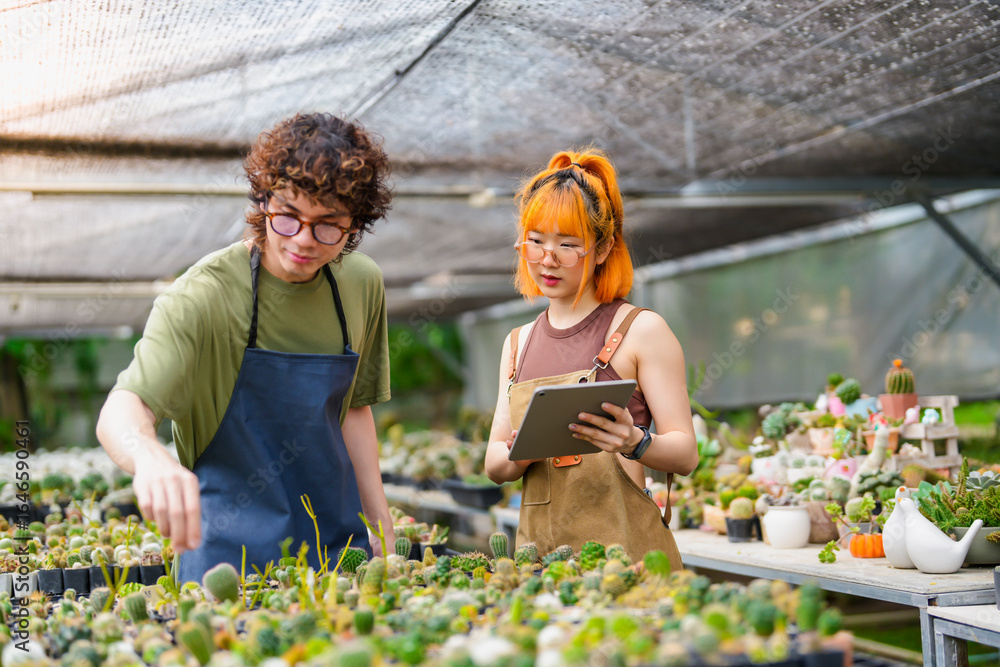 Obraz premium Young Asian Man and Woman Plant Research Working Together in Greenhouse Inspecting Blooming Cactus Flowers with Tablet Eco-Friendly Research and Data