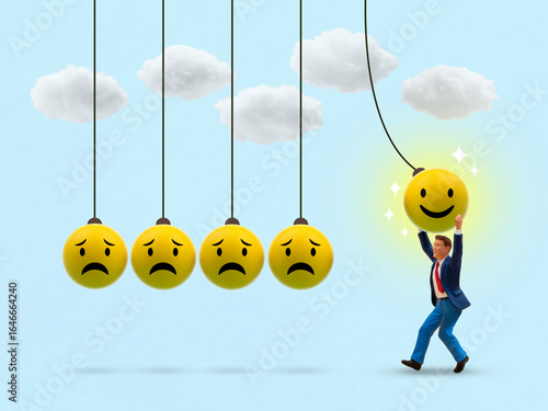A conceptual image showing a miniature man pulling a happy face ball in a Newton's cradle to transform sad faces into smiles, symbolizing positive thinking, emotional change.