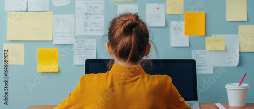 Digital marketer analyzing social media metrics on laptop with notes and sticky papers on wall, focused and working in cozy workspace