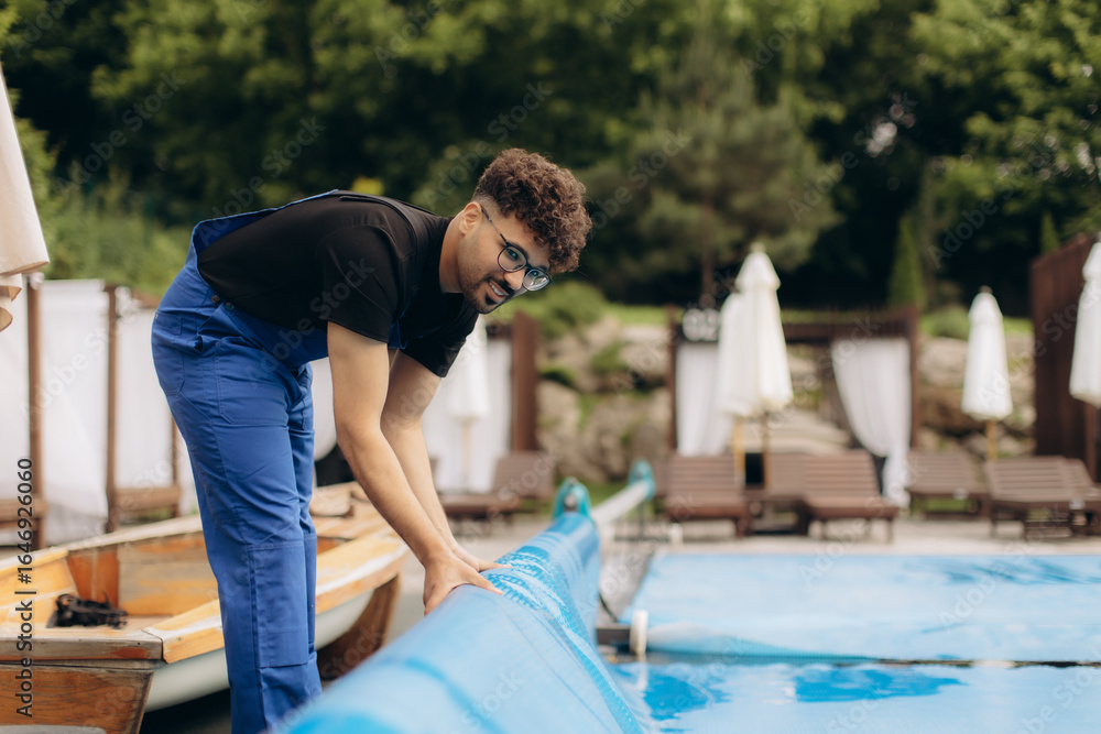 Fototapeta premium Pool maintenance worker rolling up cover at resort