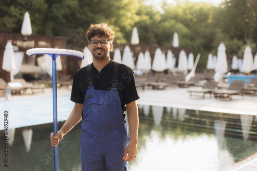 Pool cleaner holding cleaning brush and smiling by the poolside