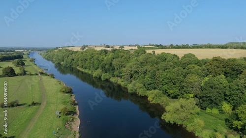 Scenic drone view over River Trent, surrounding verdant green trees and golden crops fields in Nottingham England UK