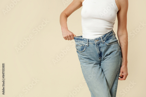 Studio shot of a young caucasian fit female wearing big jeans after diet	